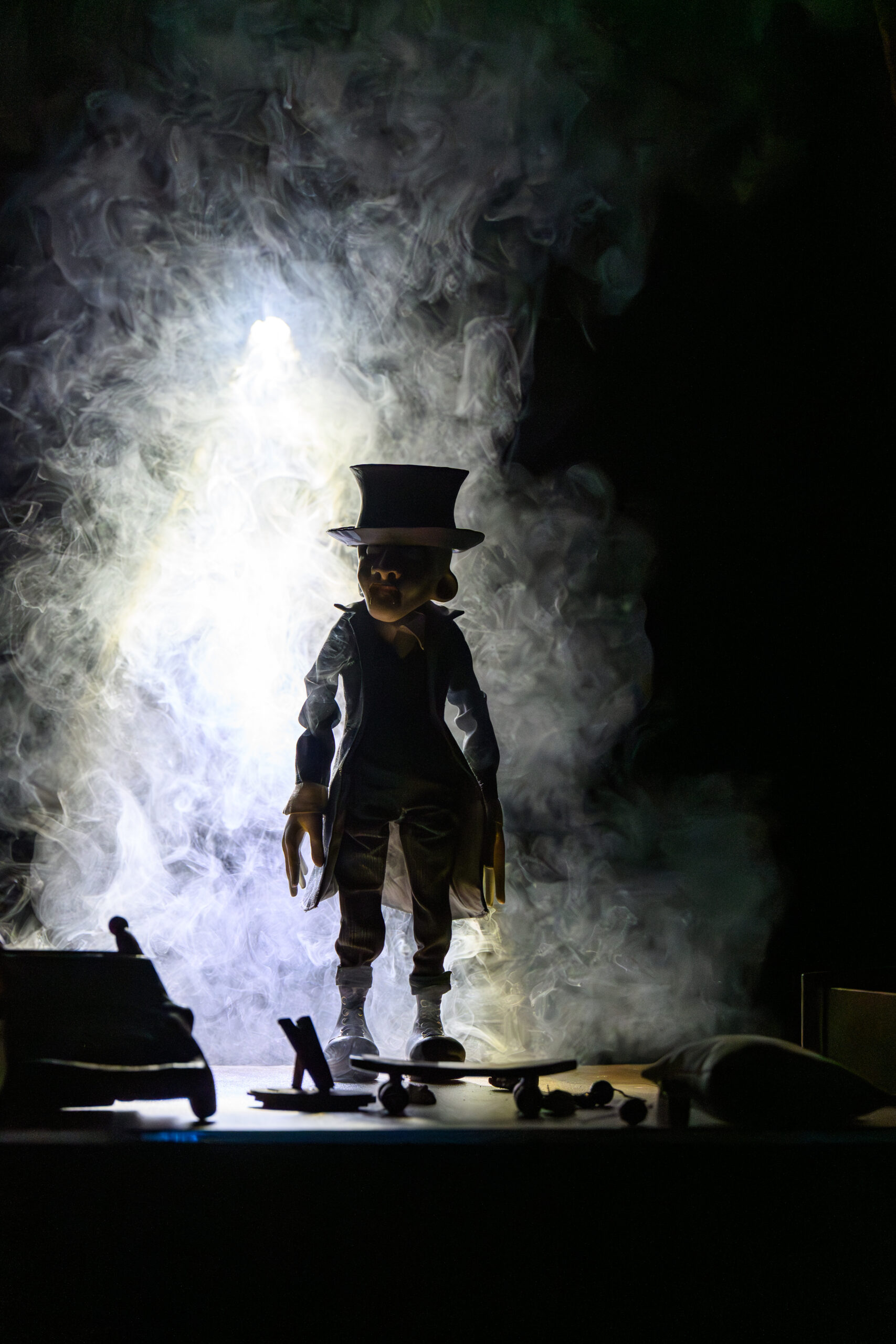 A silhouette of a ventriloquist-style puppet in a tall top hat standing in bright smoke at night, backlit scene.